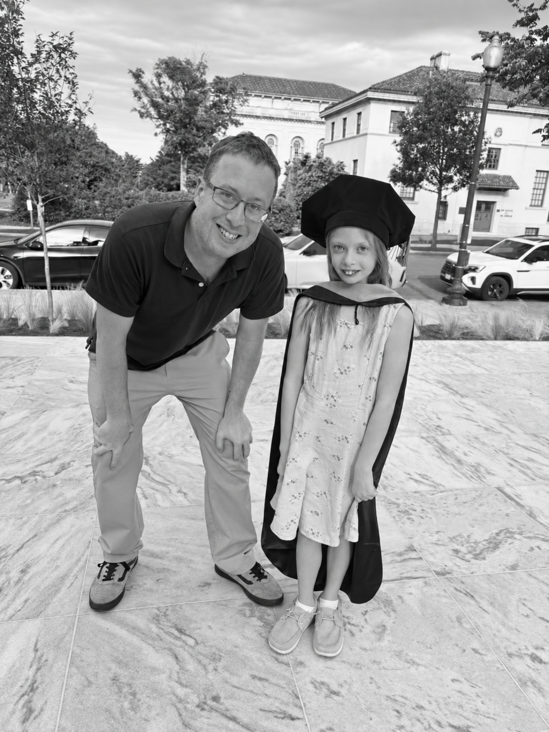 Dr. Jonathan Hammitt outdoors with a child wearing academic regalia.